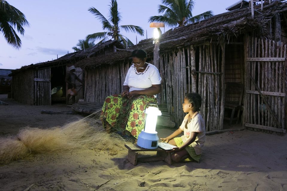 Une femme coud un filet de pêche avec sa petite-fille grâce à une lampe solaire, dans le village d’Ambakivao, à Madagascar, le 23 avril.